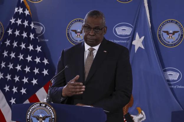 A person standing at a podium with flags behind him Description automatically generated